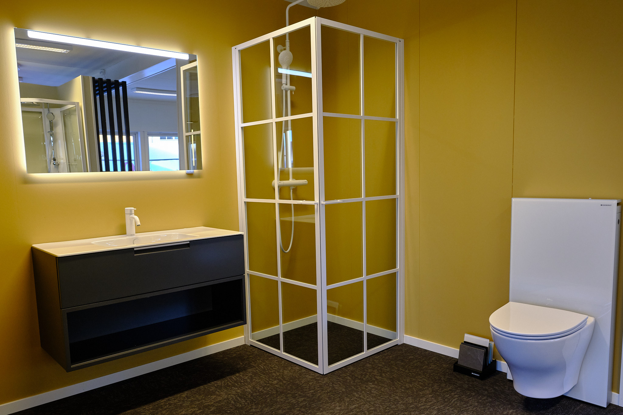 Dusjhjørne med hvite sprosser. Vegghengt toalett og sort baderomsmøbel med hvit servant og hvitt servantbatteri. Firkantet speil med lys.