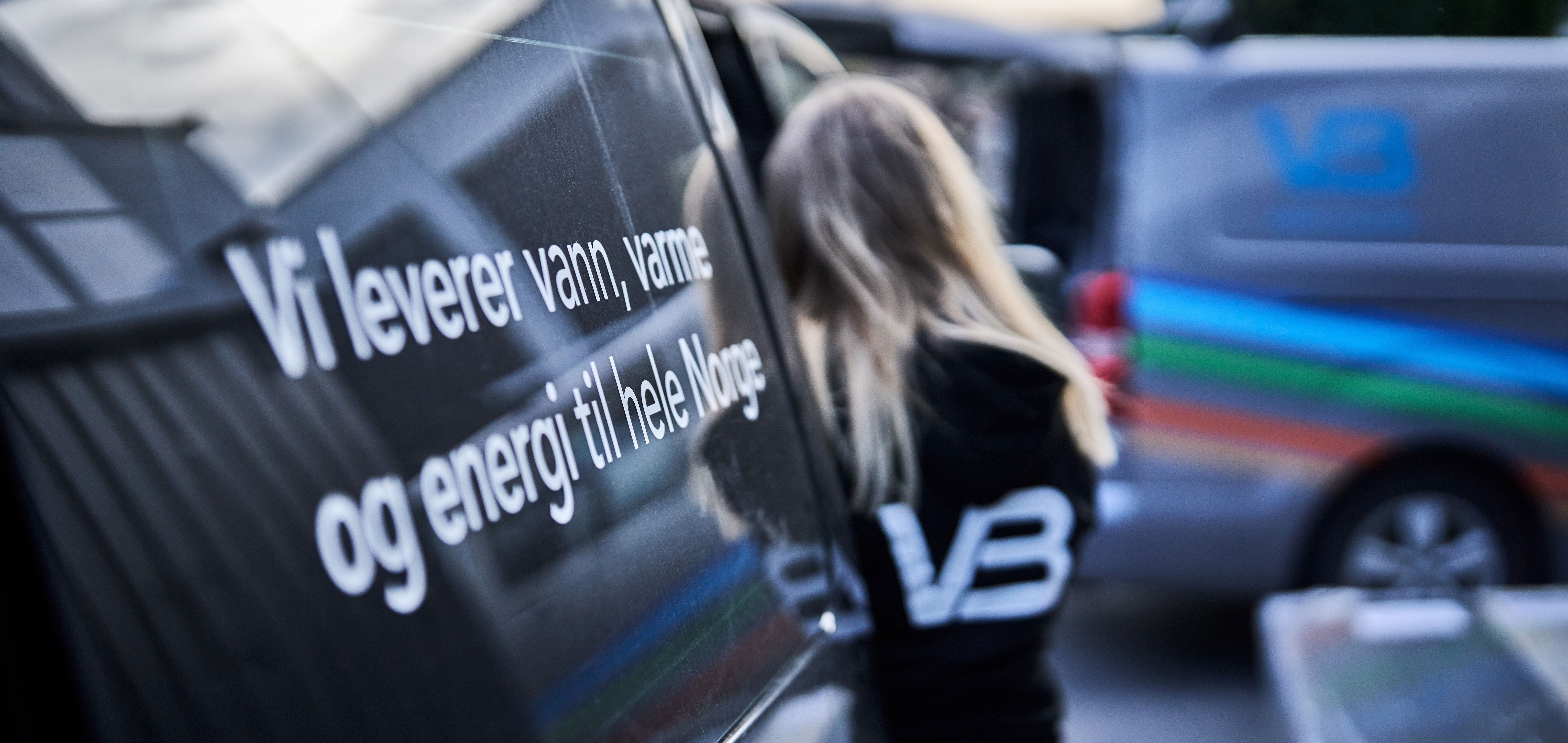 VB-rørlegger lener seg mot firmabil med profileringen "Vi leverer vann, varme og energi til hele Norge" på sideruten.